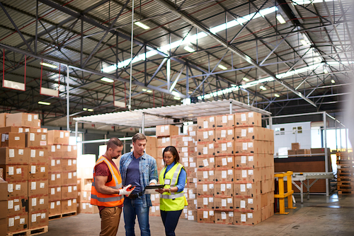 Three employees having a discussion while standing in a distribution warehouse