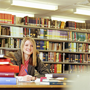 Young woman in higher education sitting at a desk in the library surrounded by schoolwork 