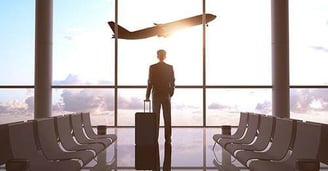 Business man standing with suitcase in front of airport window, watching a plane take off