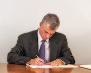 Man in a dark gray suit, sitting at a desk, looking over a buy-sell agreement